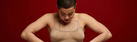 body positive, self-esteem, young woman with short hair and tattoo posing with hands on hips on burgundy background, dark red, curvy fashion, comfortable in skin, female underwear, banner