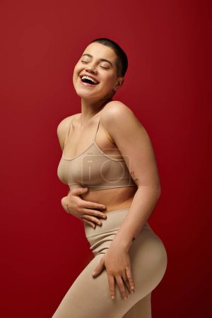 body positive, happy and tattooed woman in beige underwear pose on red background, curvy fashion, comfortable in skin, body positivity, generation z, body diversity, laughter, joy 