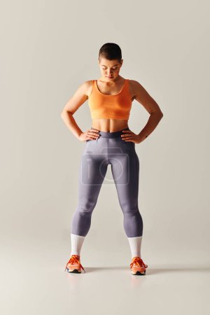 Photo for Body confidence, tattooed and short haired woman standing with hands on hips on grey background, curvy fitness model in sportswear, empowerment, motivation, working out, strength and health - Royalty Free Image