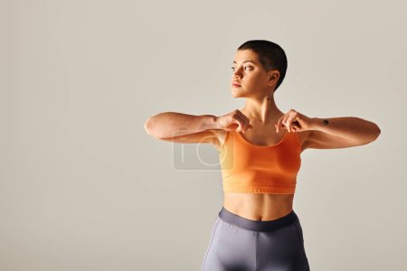 Photo for Body diversity, tattooed and short haired woman exercising and looking away on grey background, curvy fitness model in sportswear, empowerment, motivation, strength and health - Royalty Free Image