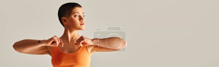 body diversity, tattooed and short haired woman exercising and looking away on grey background, curvy fitness model in sportswear, empowerment, motivation, strength and health, banner