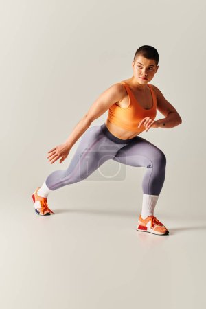Photo for Self-esteem, body positivity, young short haired woman doing lunges on grey background, curvy fitness model in sportswear, empowerment, motivation, working out, strength and health - Royalty Free Image