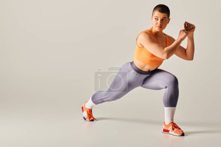 self-esteem, body positivity, young short haired woman doing lunges on grey background, curvy fitness model in sportswear, athletic and confident. empowerment, motivation, working out 