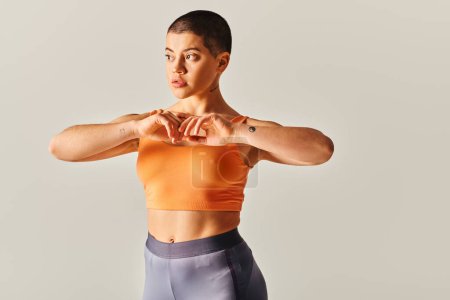 body positive, young and short haired woman exercising on grey background, curvy fitness model in sportswear, athletic and confident, empowerment, motivation, working out 