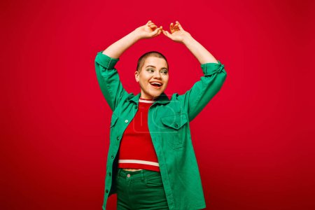 Photo for Fashion and style, excited and short haired woman in green outfit posing with raised hands on red background, generation z, youth culture, modern backdrop, individuality, personal style - Royalty Free Image