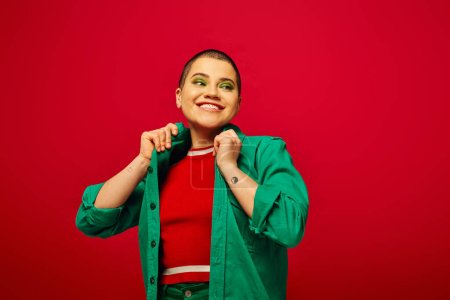 Photo for Fashion statement, happy and tattooed, short haired woman in green outfit smiling on red background, looking away, generation z, youth culture, vibrant backdrop, individuality - Royalty Free Image