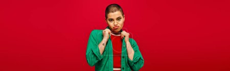 Photo for Fashion choices, emotional and tattooed, short haired woman in green outfit pouting lips on red background, looking at camera, generation z, youth culture, vibrant backdrop, style, banner - Royalty Free Image