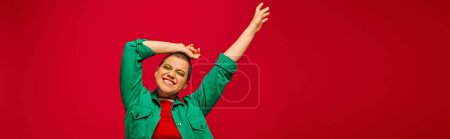 stylisches Outfit, fettes Make-up, fröhlich und tätowiert, kurzhaarige Frau im grünen Outfit posiert auf rotem Hintergrund, Generation Z, Jugendkultur, lebendiger Hintergrund, persönlicher Stil, Banner