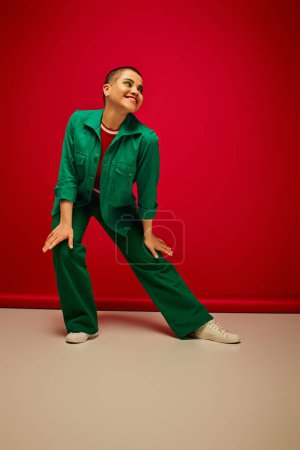 Mode-Statement, lebendige Kulisse, fröhliche und junge Frau in stilvoller Kleidung posiert auf rotem Hintergrund, volle Länge, Generation z, Jugendkultur, persönlicher Stil, kurvige Mode 