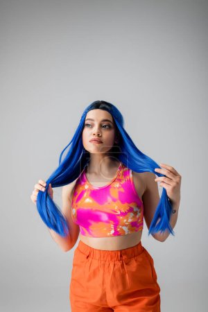 énergie jeune, jeune femme tatouée aux cheveux bleus posant en vêtements colorés sur fond gris, individualisme, style moderne, mode urbaine, couleur vibrante, déclaration de mode 