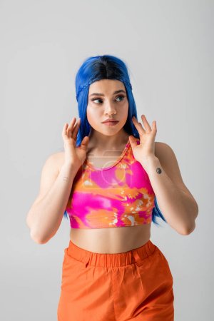 modern individual, tattooed young woman with blue hair posing with hands near face on grey background, modern style, urban fashion, vibrant color, female model, looking away