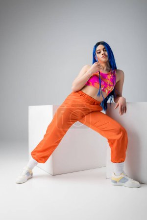 modern subculture, tattooed woman with blue hair posing in colorful clothes near white cubes on grey background, full length, individualism, modern style, urban fashion, vibrant color, young model 
