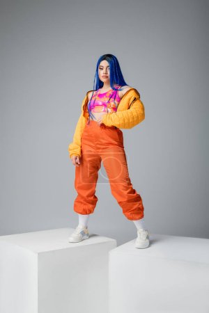 beauty and fashion trends, young tattooed woman with blue hair posing in colorful clothes on grey background, full length, white cubes, individualism, modern style, urban fashion, vibrant color 
