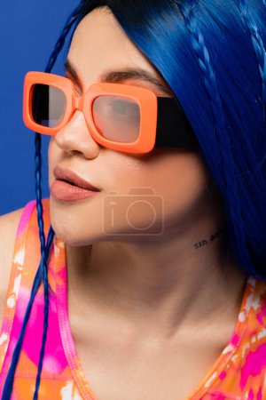 retrato, accesorio de moda, modelo femenino joven con pelo azul y gafas de sol de moda aisladas sobre fondo azul, generación z, estilo rebelde, ropa colorida, individualismo, mujer moderna 