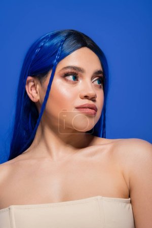 Foto de Piel brillante, mujer joven con el pelo teñido posando sobre fondo azul, color de pelo, individualismo, modelo femenino con maquillaje y peinado de moda, juventud vibrante, perfección de la piel - Imagen libre de derechos