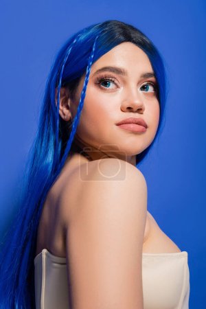 Foto de Fotografía de belleza, mujer joven con el pelo teñido posando sobre fondo azul, color de pelo, piel brillante, modelo femenino con maquillaje y peinado de moda, juventud vibrante, perfección de la piel - Imagen libre de derechos