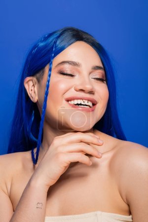 Photo for Beauty concept, happy young woman with dyed hair posing on blue background, hair color, individualism, female model with makeup and trendy hairstyle smiling with closed eyes, vibrant youth - Royalty Free Image