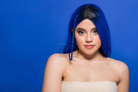 Foto de Concepto de belleza moderna, mujer joven con el pelo teñido posando sobre fondo azul, color de pelo, individualismo, modelo femenino con maquillaje y peinado de moda, juventud vibrante, perfección de la piel - Imagen libre de derechos