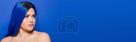Porträt einer unzufriedenen Frau mit gefärbten Haaren, die auf blauem Hintergrund wegschaut, Haarfarbe, Individualismus, weibliches Model mit Make-up und trendiger Frisur, lebendige Jugend, emotional, Banner 
