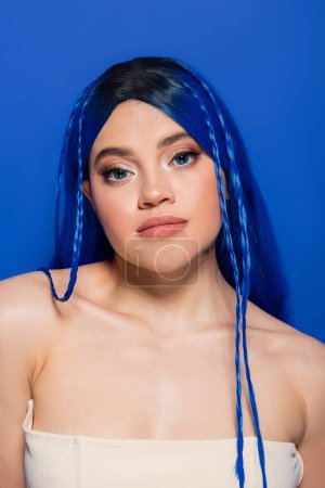 Schönheitskonzept, junge Frau mit gefärbten Haaren und glühender Haut posiert auf blauem Hintergrund, Haarfarbe, Individualismus, weibliches Model mit Make-up und trendiger Frisur, lebendige Jugend, Perfektion der Haut 