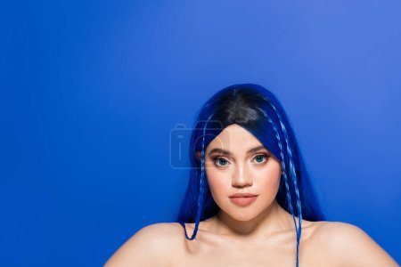 Individualismus, Porträt einer jungen Frau mit gefärbten Haaren und glühender Haut, die auf blauem Hintergrund posiert, Haarfarbe, Individualismus, weibliches Model mit Make-up und trendiger Frisur, lebendige Jugend 