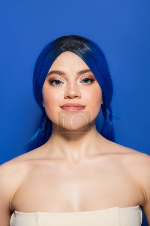 Leuchtendes Hautkonzept, Porträt einer selbstbewussten jungen Frau mit lebendigem Haar, die mit nackten Schultern auf hellblauem Hintergrund posiert, Jugend, Individualismus, Schönheitstrends, einzigartige Identität, Blick in die Kamera