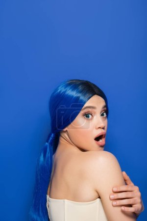 modelo emocional, retrato de mujer joven conmocionada con color de pelo vibrante posando con hombros desnudos sobre fondo azul, juventud, tendencias de belleza, identidad única, bandera