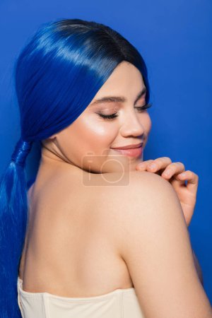 concepto de piel brillante, retrato de mujer joven feliz con color de pelo vibrante posando con hombros desnudos sobre fondo azul brillante, juventud, individualismo, tendencias de belleza, identidad única 
