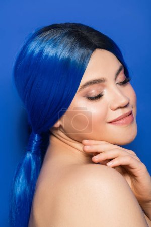 glowing skin concept, portrait of young woman with vibrant hair color posing with bare shoulders on blue background, youth, individualism, beauty trends, unique identity, closed eyes