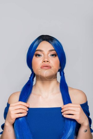beauty trends, dyed hair, female model looking at camera, portrait of tattooed woman with bare shoulders posing in bright blouse on grey background, blue hair color, hairstyle, makeup and beauty 