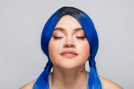 moderne Subkultur, tätowierte Frau mit geschlossenen Augen und blauen Haaren, die auf grauem Hintergrund posiert, Frisur, lebendige Farbe, moderne Schönheit, Selbstausdruck, Individualismus 