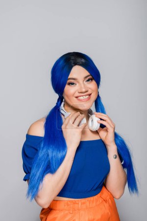 Photo for Music lover, cheerful young woman with blue hair and wireless headphones smiling on grey background, vibrant youth, individualism, modern subculture, self expression, tattoo, sound - Royalty Free Image