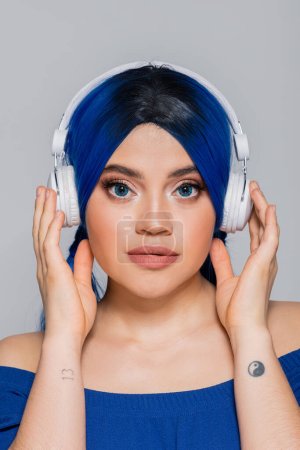 Musikliebhaberin, junge Frau mit blauen Haaren, die Musik in drahtlosen Kopfhörern auf grauem Hintergrund hört, lebendige Jugend, Individualismus, moderne Subkultur, Selbstausdruck, Tätowierung, Sound 