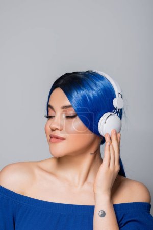 Selbstausdruck, Musikliebhaber, junge Frau mit blauen Haaren, die Musik in drahtlosen Kopfhörern auf grauem Hintergrund hört, geschlossene Augen, lebendige Jugend, Individualismus, moderne Subkultur, Tätowierung, Sound 