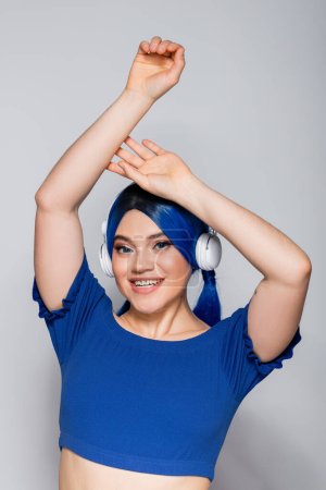 self expression, happy young woman with dyed hair listening music in wireless headphones on grey background, vibrant youth, individualism, modern subculture, tattoo, sound 