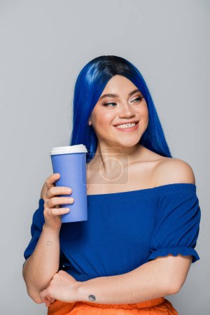 Foto de Positividad, taza desechable, mujer joven con cabello azul y ojos sosteniendo café para ir sobre fondo gris, comida para llevar, cafeína, energía, tatuaje, color vibrante, expresión personal, individualismo - Imagen libre de derechos