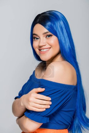 positivity and beauty trends, tattooed young woman with dyed hair smiling on grey background, hairstyle, blue hair, modern beauty, self expression, individualism, makeup and glowing skin 