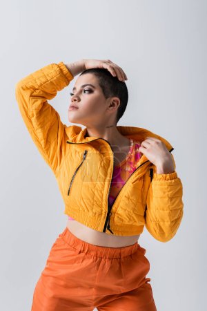 outerwear, fashion statement, fashion model looking away, young woman with short hair posing in yellow puffer jacket on grey background, isolated, youth culture, casual wear, stylish look 