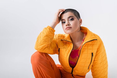 urban fashion, outerwear, female model posing in casual attire, young woman with short hair and puffer jacket sitting on grey background, looking at camera, personal style, self expression 