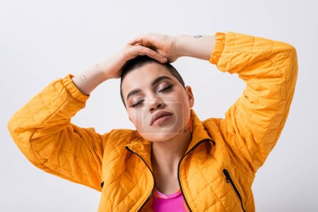 fashion statement, tattooed young woman in colorful clothes sitting with closed eyes on grey background, urban style, individualism, vibrant and youthful energy, stylish look, outerwear 
