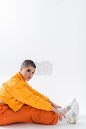 stylish look fashion statement, tattooed young woman in colorful clothes sitting on grey background, urban style, individualism, vibrant and youthful energy, urban fashion, generation z