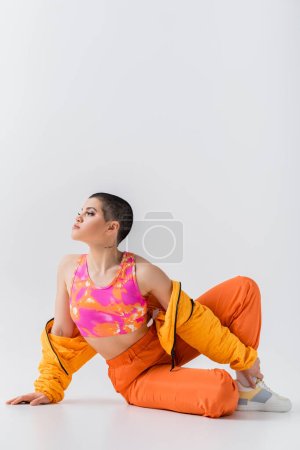 vibrant youth, tattooed young woman with short hair sitting on grey background, generation z, fashion forward, colorful clothes, female model with personal style, self expression, trendy outfit 
