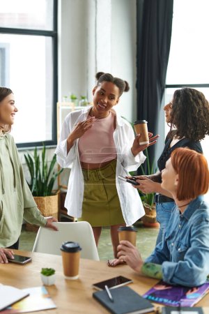 Photo for Delighted african american woman holding takeaway coffee and showing new jewelry necklace to positive multicultural girlfriends in interest club, happy gathering and leisure of diverse female team - Royalty Free Image
