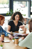 young woman pointing at magazine near smiling multicultural girlfriends and paper cups with coffee to go on table in women club, common interests and knowledge-sharing concept puzzle #664266770