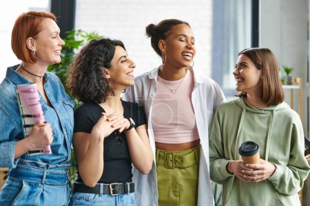 junge und glückliche Frau mit Coffee to go beim Anblick stilvoller multiethnischer Freundinnen, die im Fraueninteressenclub stehen und lachen, gegenseitige Unterstützung, Solidarität und Vertrauenskonzept