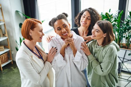 positive psychologist and multiracial female friends hugging pleased african american woman during psychological coaching, moral support and mental wellness concept
