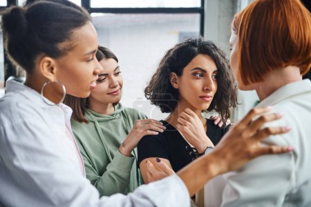 offended multiracial woman looking away near multicultural female friends and psychologist calming her in consulting room, problem-solving and mutual support concept