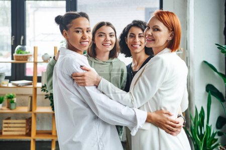Photo for Optimistic and joyful multicultural female friends with redhead motivation coach embracing and smiling at camera in consulting room, female unity and support concept - Royalty Free Image