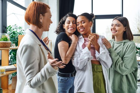 Photo for Cheerful multiethnic women embracing african american girlfriend near happy motivation coach gesturing in consulting room, female unity and support concept - Royalty Free Image