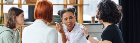 mujer afroamericana molesta hablando con entrenador de motivación y amigas multiculturales durante la sesión de psicología en la sala de consulta, la resolución de problemas y el concepto de bienestar mental, pancarta